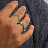 hand wearing 5mm blue diamond ring with 4mm round cut prong-lifted stones on textured dark fabric background