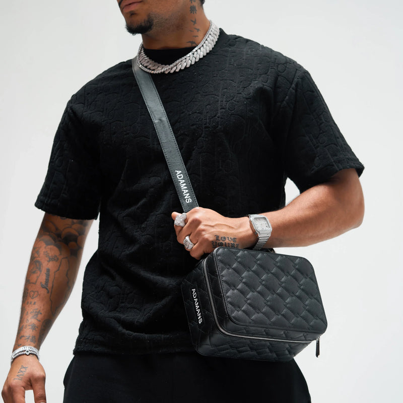 black leather travel jewellery case with adjustable shoulder strap and quilted design worn crossbody by tattooed man in black shirt