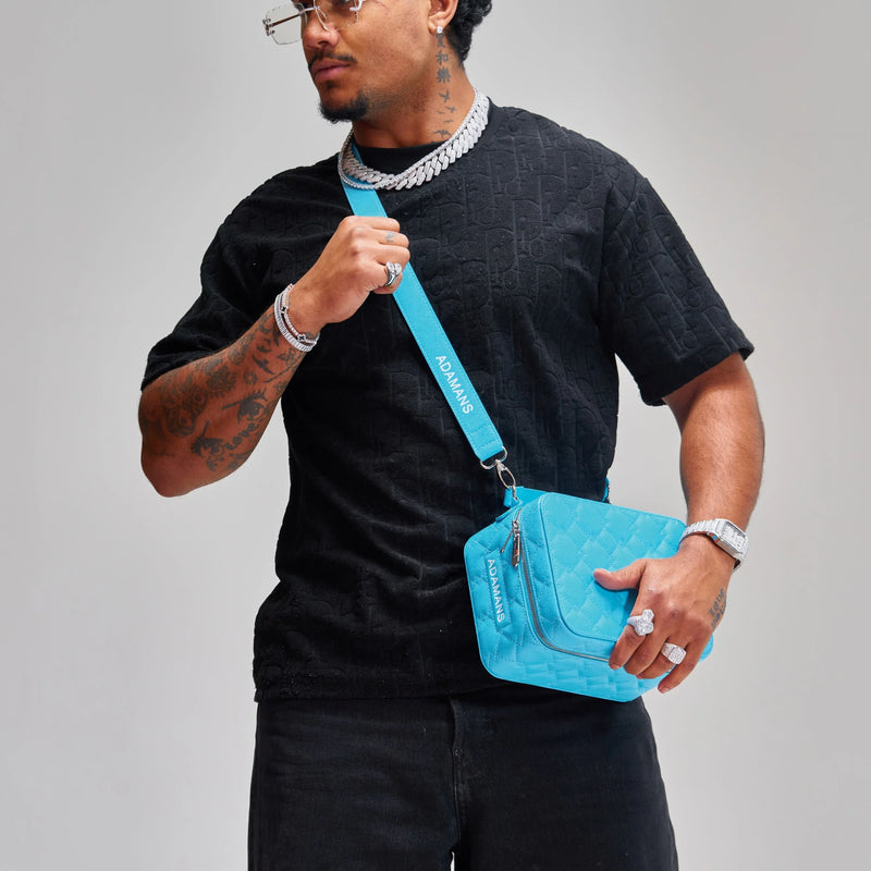 man wearing black outfit holding blue small leather travel jewellery case with adjustable strap
