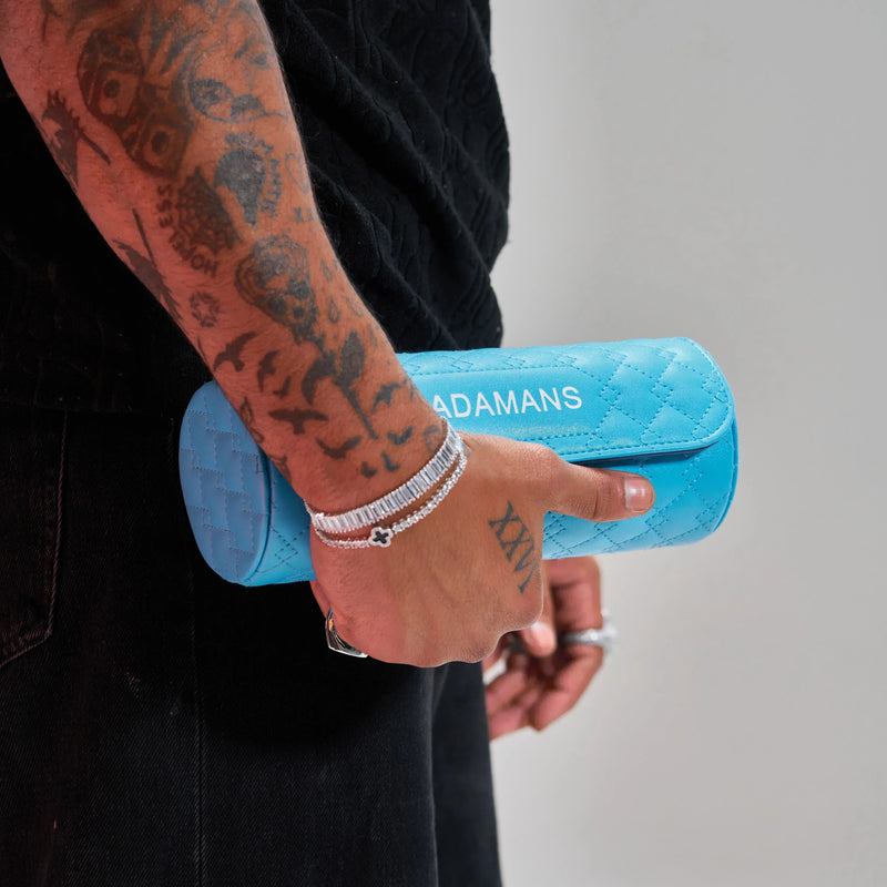 Blue leather travel watch roll by Adamans held in hand with tattooed arm and silver bracelets