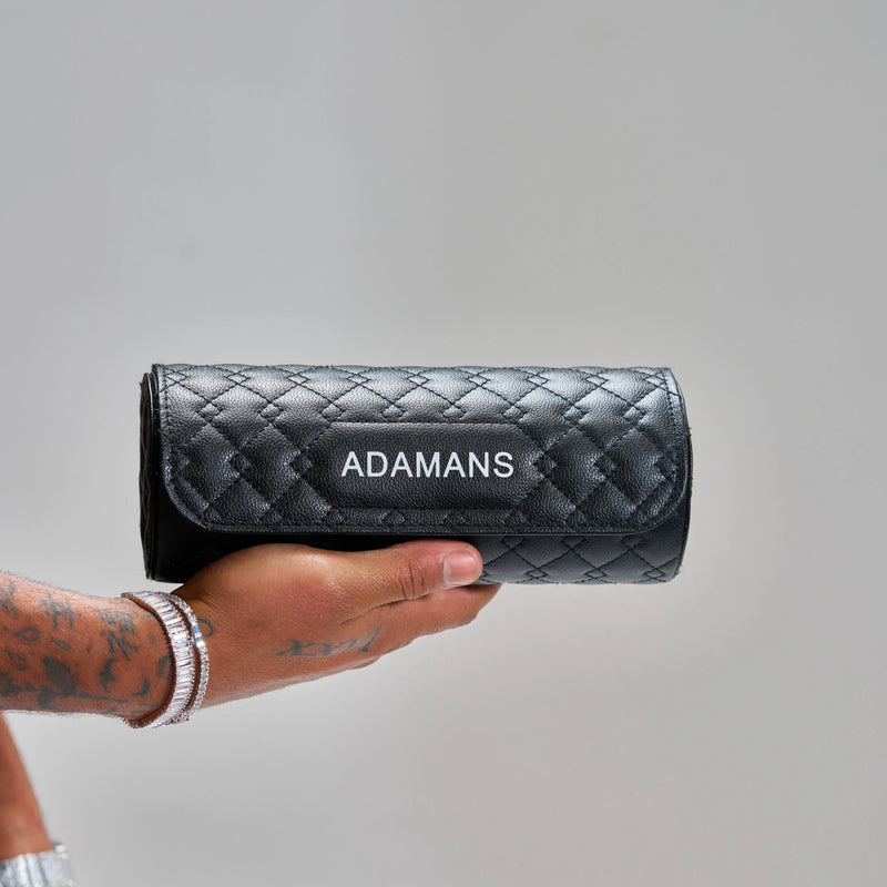 Black leather travel watch roll by Adamans with quilted design and adjustable shoulder strap, ideal for organizing and protecting jewelry.