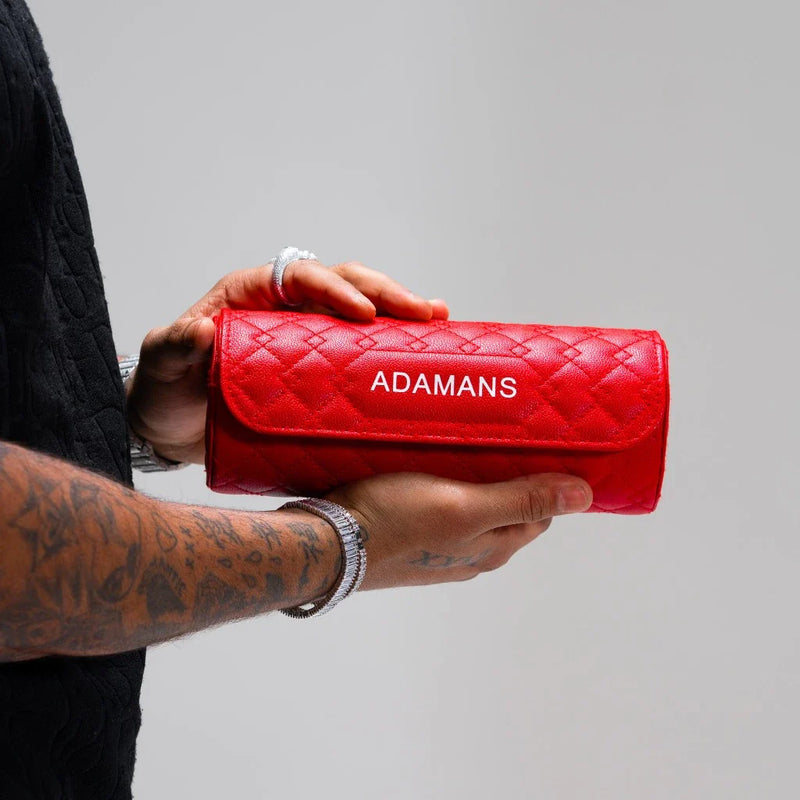 Red leather travel watch roll by Adamans held in hands with tattooed forearms and grey background