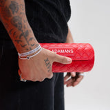 Red leather travel watch roll with quilted design and adjustable shoulder strap by Adamans held in hand