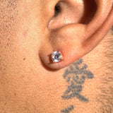Close-up of moissanite stud earring in rose gold setting on ear with tattoo background