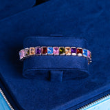 Colored cut tennis bracelet in white gold with multicolored gemstones on blue velvet display