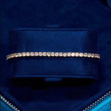 3mm gold tennis bracelet with prong-lifted round cut diamond simulants on navy blue display cushion