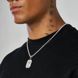 Close-up of man wearing white gold palm tree pendant necklace on silver chain against black shirt