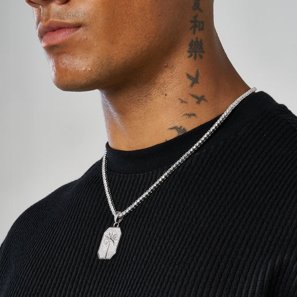 Close-up of man wearing white gold palm tree pendant necklace on silver chain against black shirt
