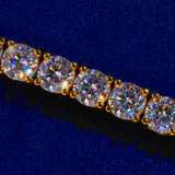 Close-up of a 5mm gold tennis bracelet with round cut prong-lifted diamond simulant stones on a blue background