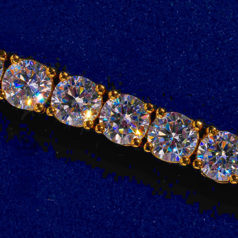 Close-up of a 5mm gold tennis bracelet with round cut prong-lifted diamond simulant stones on a blue background