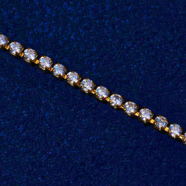 Close-up of gold micro tennis bracelet with round cut diamond simulant stones on dark blue background